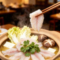 Thin slices of raw sea bass fillet held in chopsticks over a hot pot